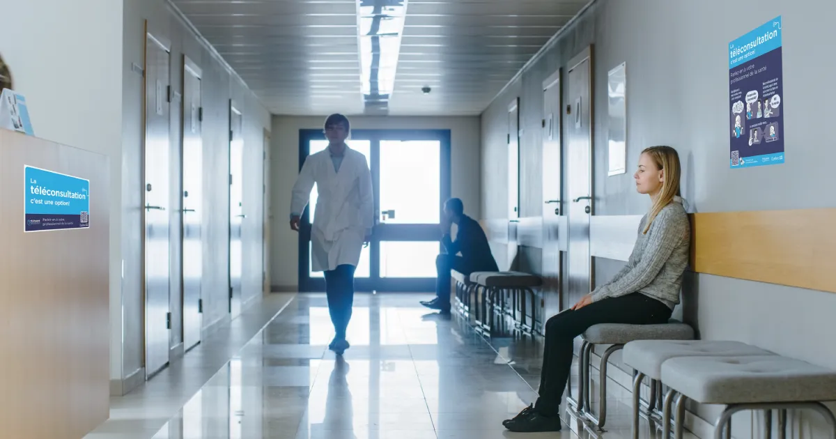 Aire d’attente dans un hôpital avec des usagers, un médecin et les affiches de la campagne La téléconsultation, c’est une option! au mur. 
